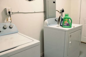 Ein Waschbereich mit einer Waschmaschine und einem Trockner, einer Steckdose und einer Flasche Gain Waschmittel auf dem Trockner.