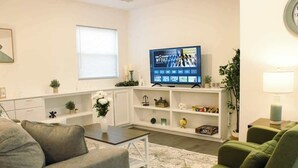 Ett vardagsrum med en tv, en soffa, ett soffbord och en bokhylla.