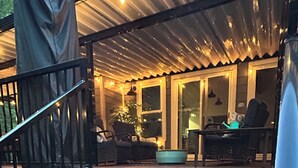 Puinen portaikko johtaa katettuun ulkotilaan, jossa on istuimia ja pöytä.