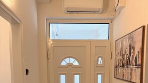 Un pasillo con una puerta blanca, un ventanal pequeño y un cuadro en la pared.