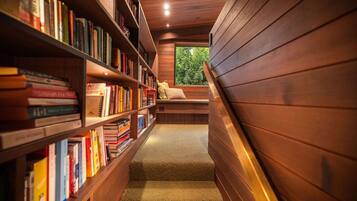 A narrow, wooden interior with bookshelves on one side and a bench with cushions on the other.