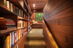 A narrow, wooden interior with bookshelves on one side and a bench with cushions on the other.