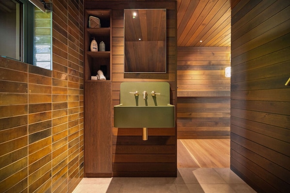 A bathroom with a green sink, wooden paneling, and a shelf with toiletries.