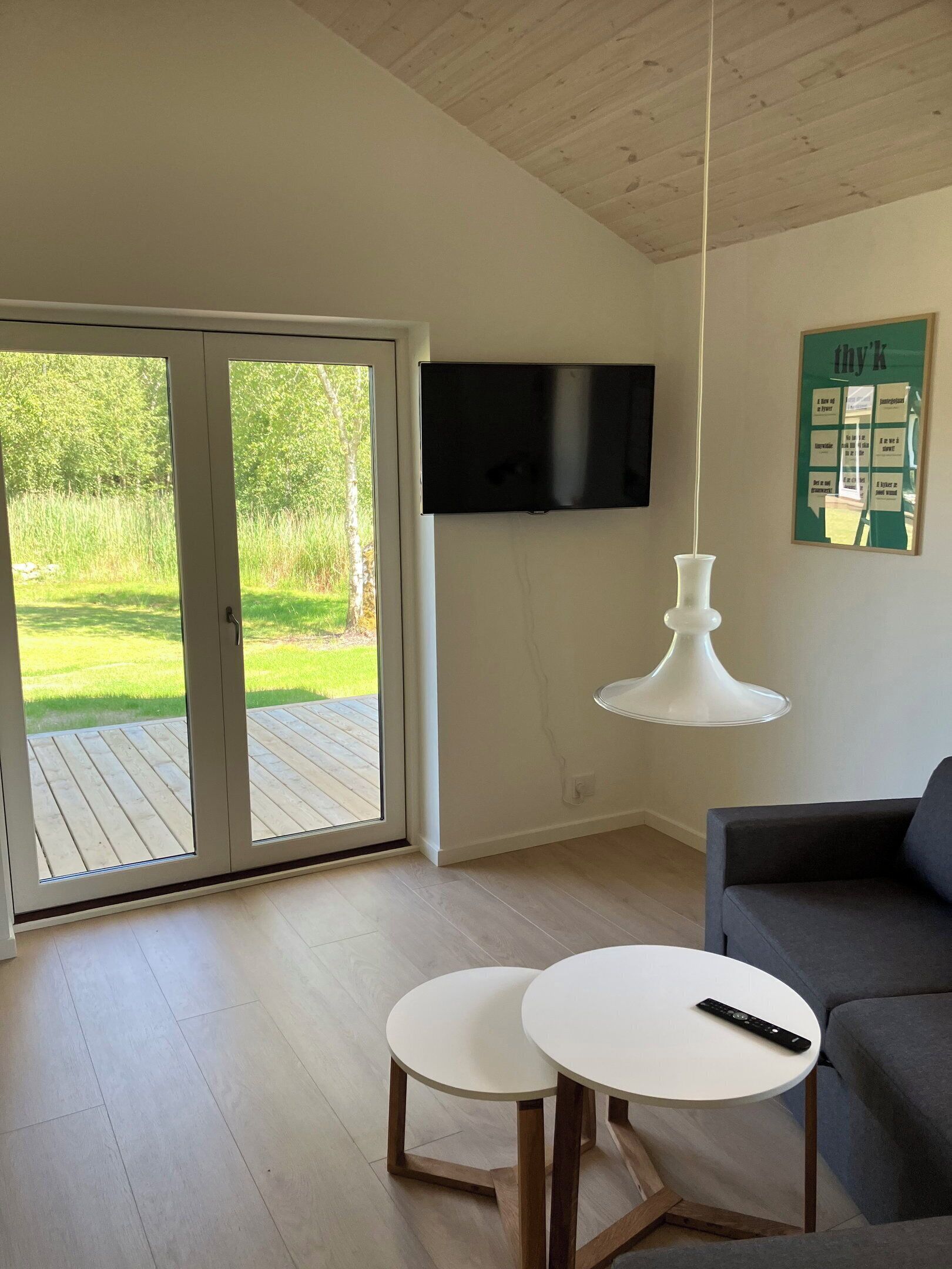 Een woonkamer met een televisie, een witte tafel, een grijze bank en een glazen schuifdeur naar een terras.