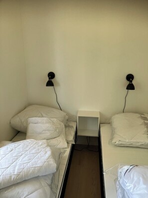 Ein Zimmer mit zwei Betten, jeweils mit weißer Bettwäsche und einer schwarzen Wandlampe.