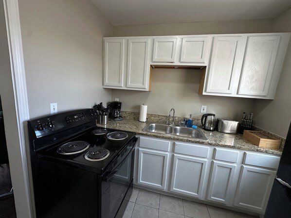 A kitchen with white cabinets, a black stove, a sink, and various kitchen items.