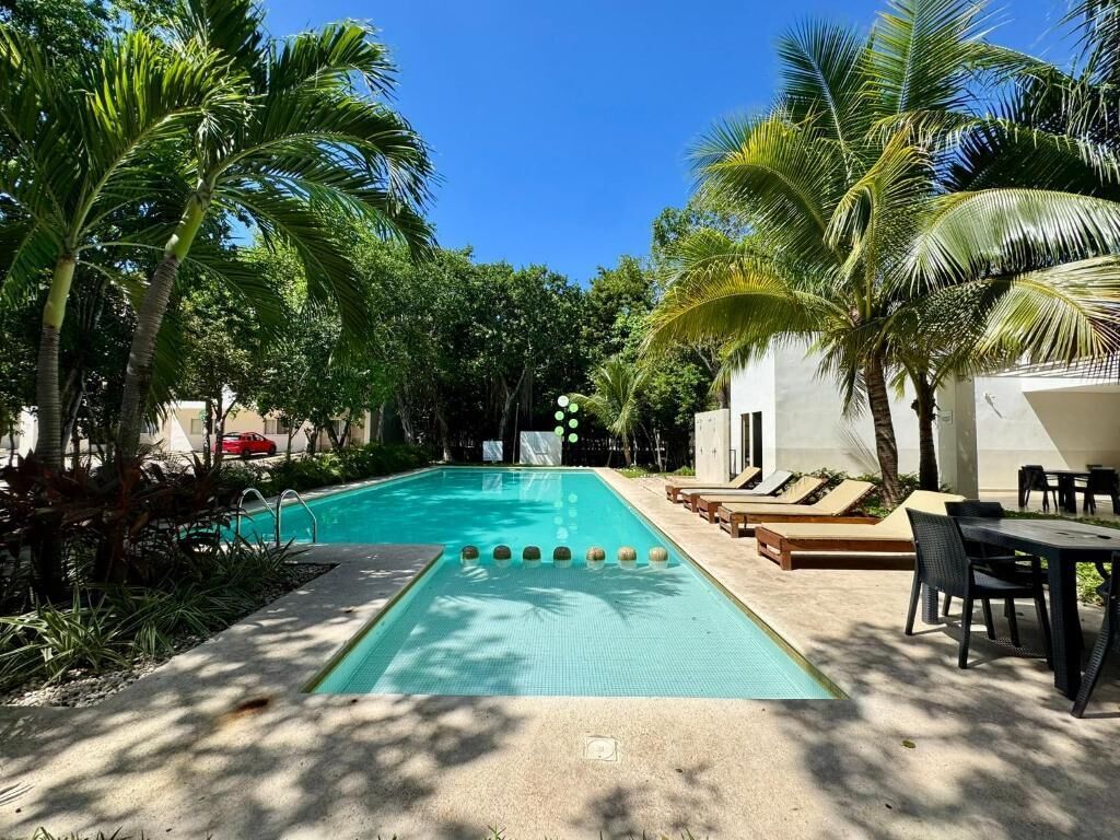 Une piscine entourée de palmiers, avec des chaises longues et des tables.