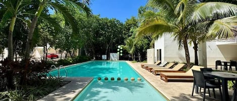 A swimming pool with lounge chairs and tables, surrounded by palm trees.