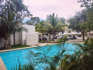 A swimming pool surrounded by palm trees and a white building with multiple windows. - FAMILY-FRIENDLY PRIVATE APARTMENT JUST 15 MINUTES AWAY FROM 5TH AVE AND THE BEACH. SELF-CHECK-IN (Playa del Carmen)