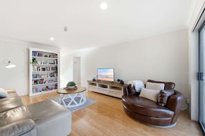 A modern living room with a leather sofa, a white bookshelf, a flat-screen TV, and a wooden coffee table. - Stylish 2-Bed Apartment in Kingston (Kingston)