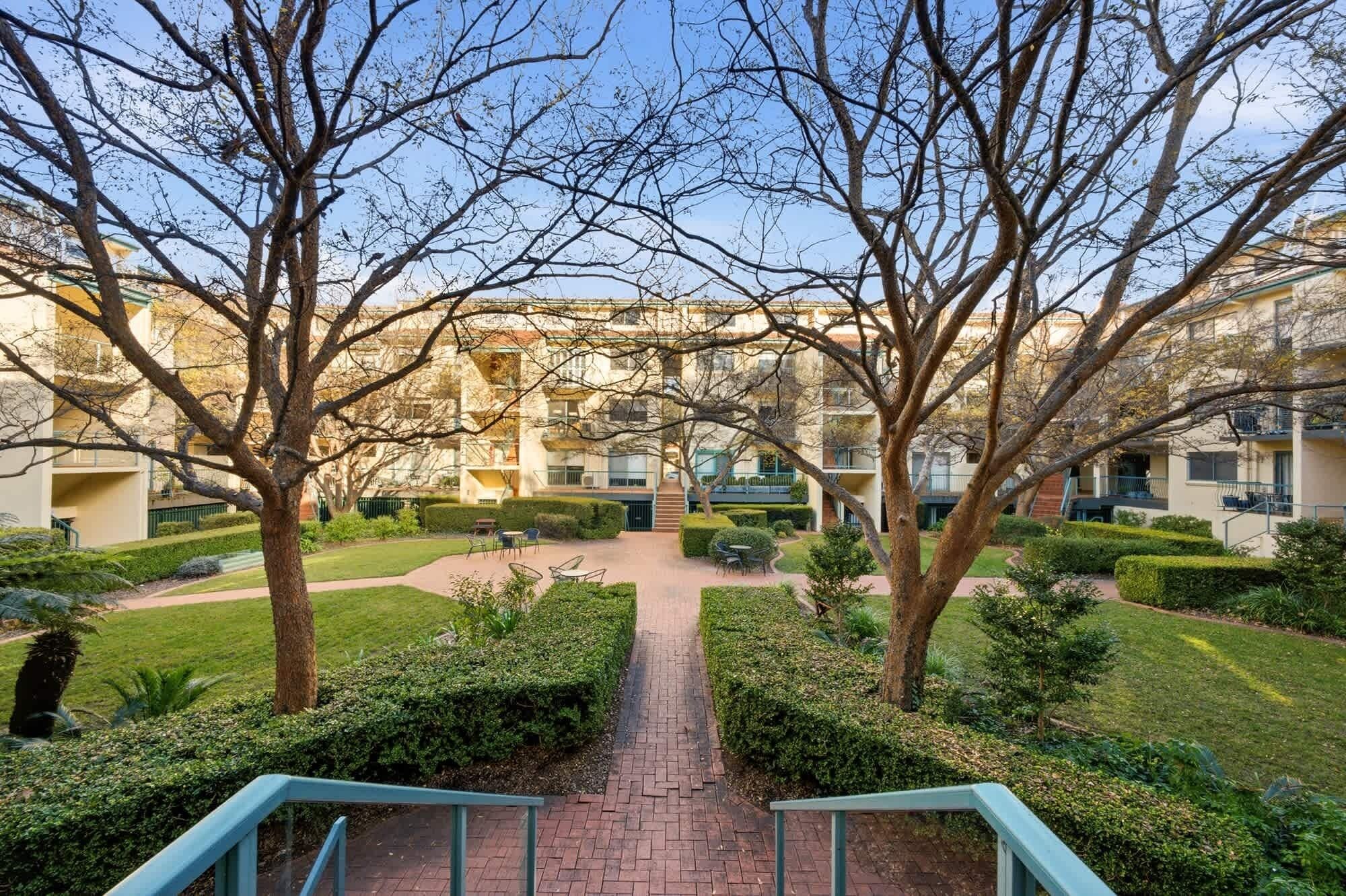 Un patio central con un sendero, rodeado de árboles y un edificio con varios balcones.
