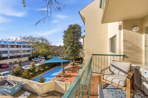 A balcony with a view of a swimming pool, a chair, and a building with a blue roof. - Stylish 2-Bed Apartment in Kingston (Kingston)