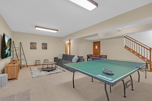 A living room with a ping pong table, a sofa, a coffee table, and a television.