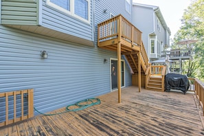 A deck with a wooden staircase leading to a second-story deck, a covered outdoor seating area, and a hose on the deck floor.