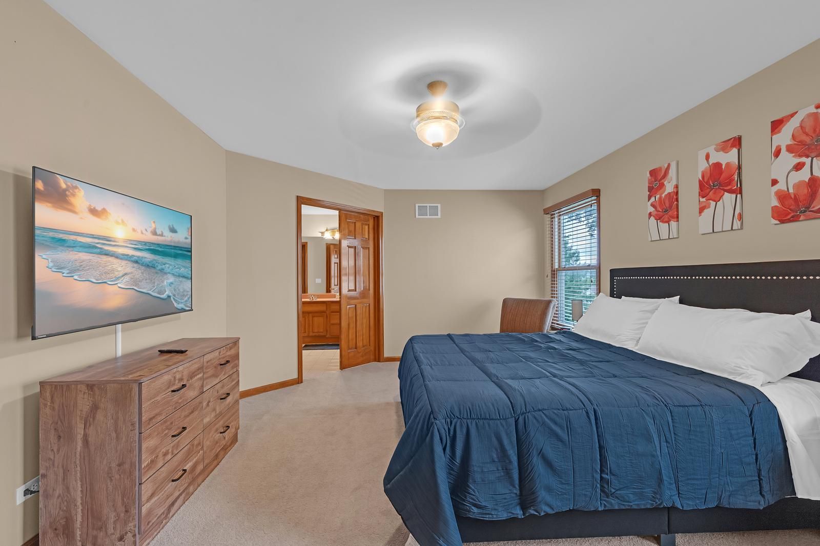 A bedroom with a bed, a dresser, a television, and a ceiling fan.