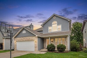 A two-story house with a garage, a basketball hoop, and a well-maintained lawn.