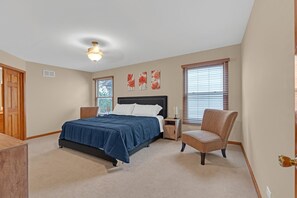 A bedroom with a bed, a chair, a nightstand, and a ceiling fan.