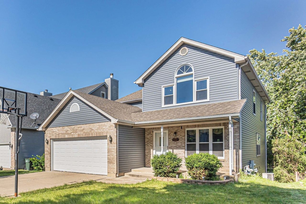A two-story residential house with a garage, a front porch, and a small front yard.
