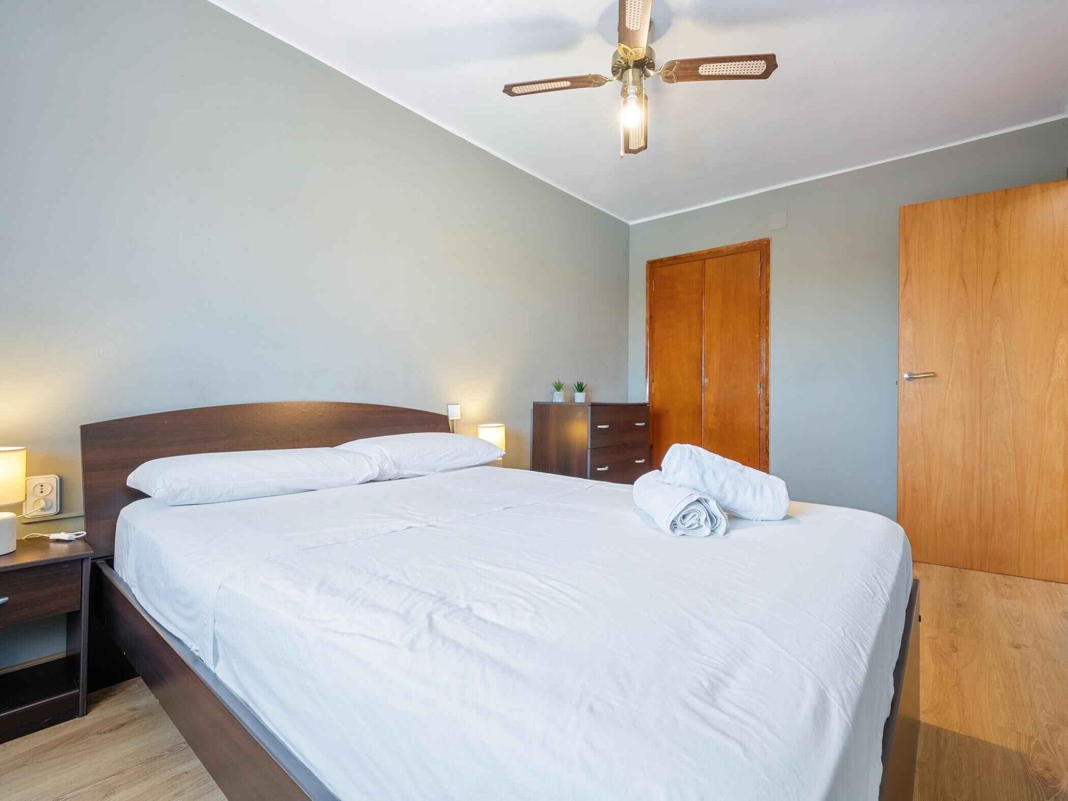 A hotel room with a bed, bedside lamps, a wooden wardrobe, and a ceiling fan.