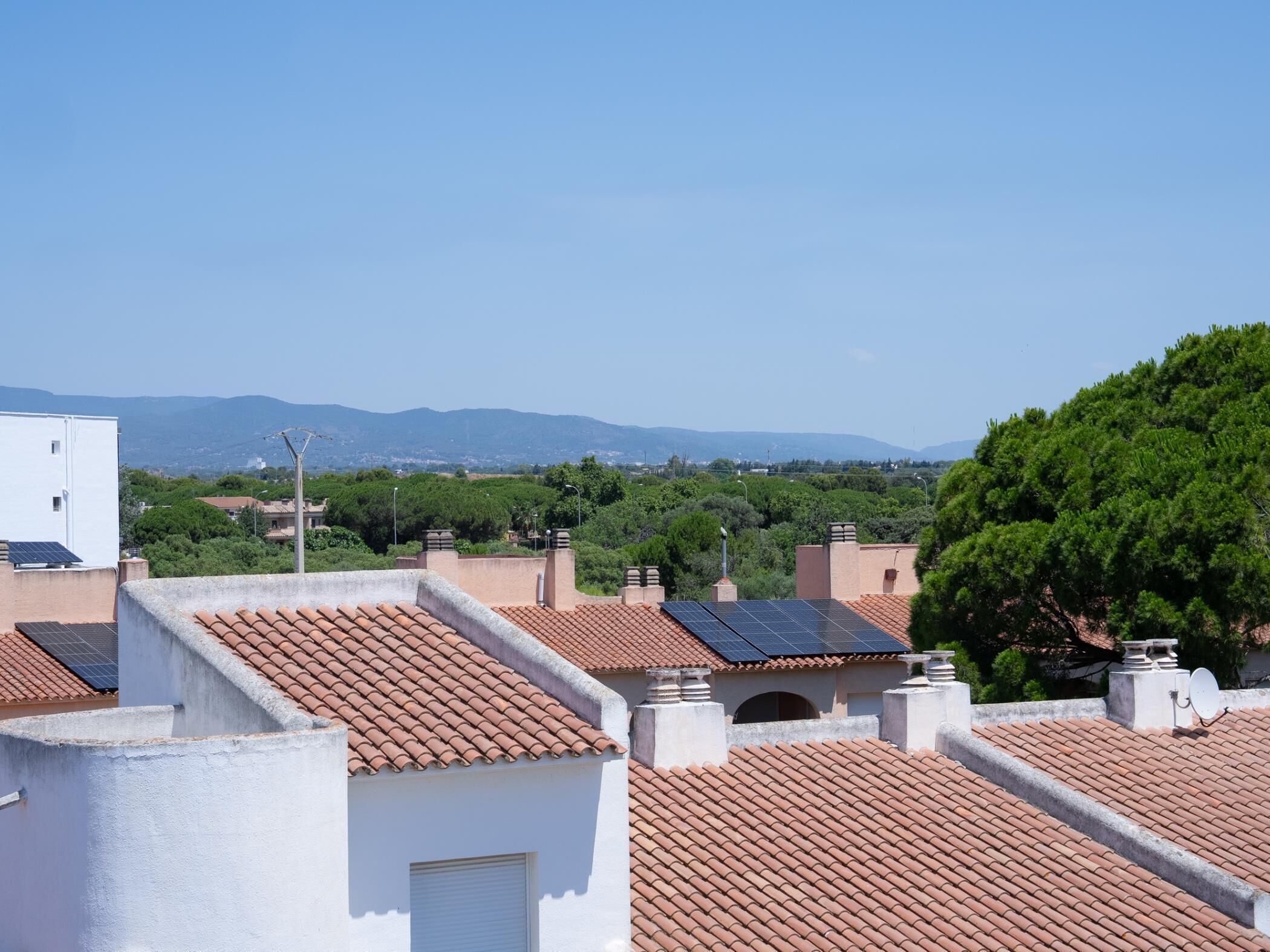 Zona residencial con tejados de tejas rojas y algunas con paneles solares, y una vista despejada de colinas distantes.
