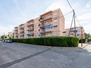 Een meerlaags woongebouw met balkons, een heldere lucht en geparkeerde auto's langs de straat.