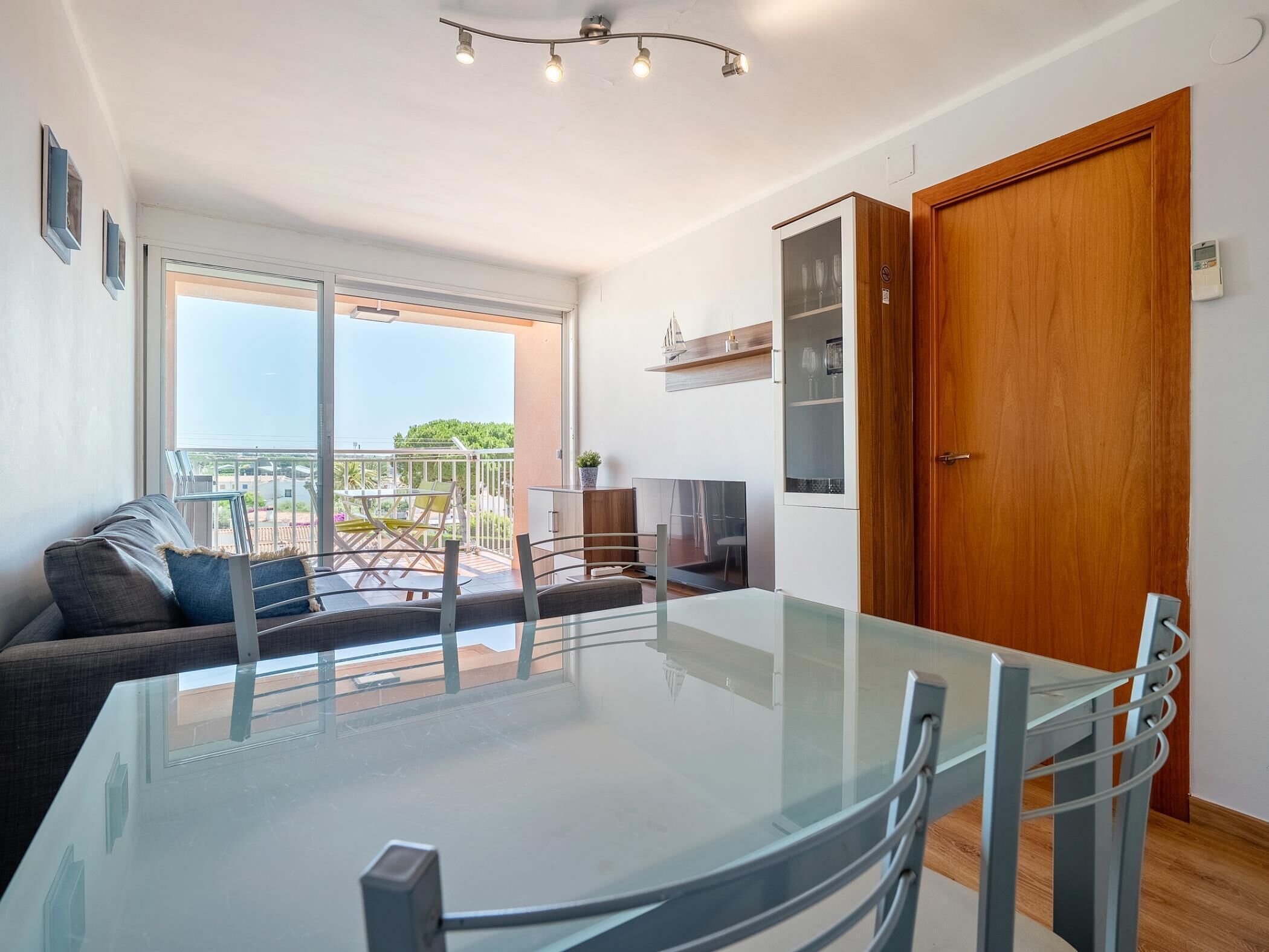 A modern living room with a glass dining table, a sofa, and a balcony with outdoor furniture.