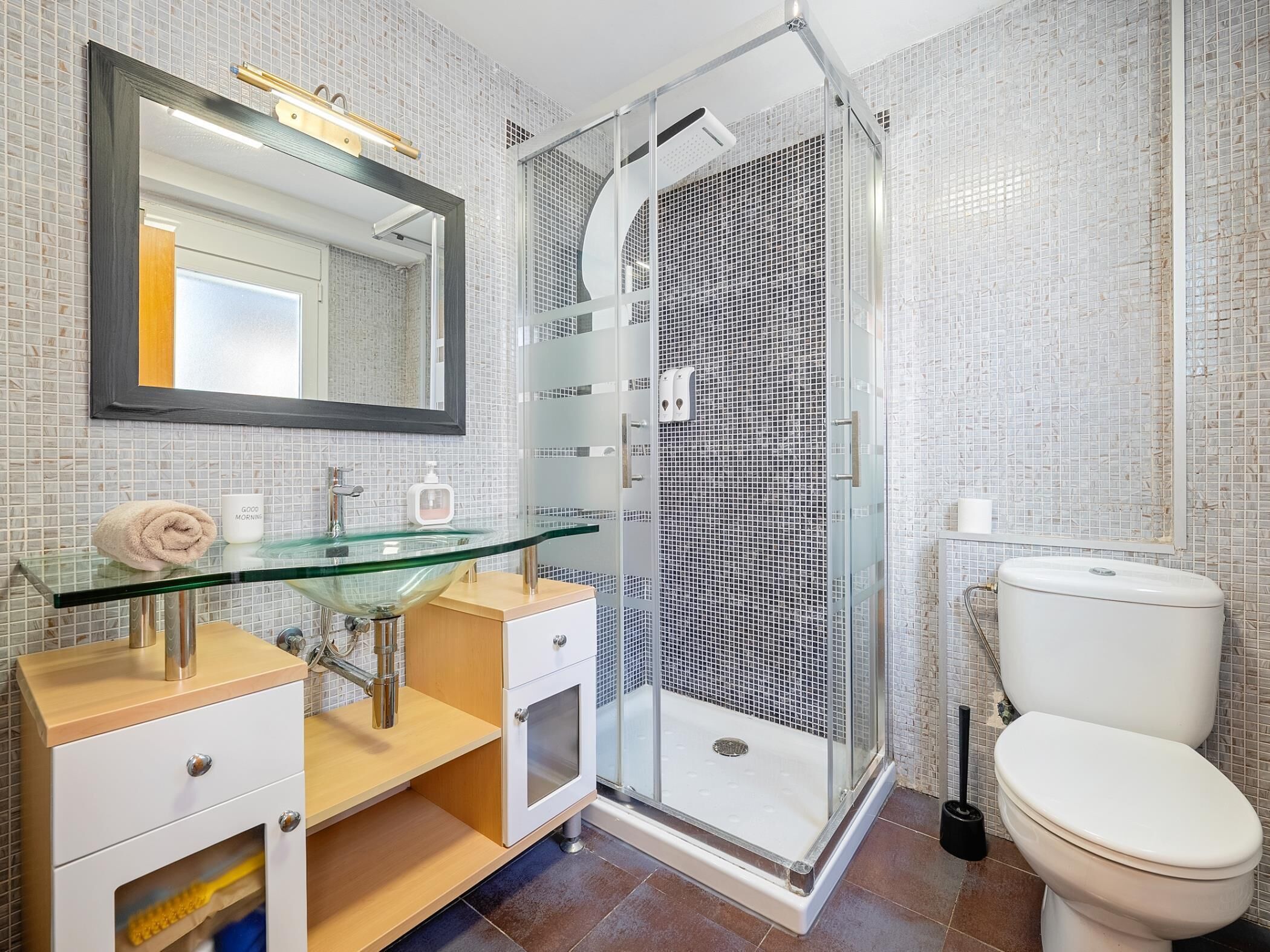 Un baño moderno con lavamanos de vidrio, ducha a ras de suelo y inodoro.
