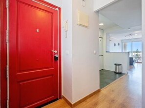 A red door with a keyhole, a white wall with a light switch, and a glimpse of a modern kitchen with a trash bin. - Apartment with terrace 400m beach (Cambrils)