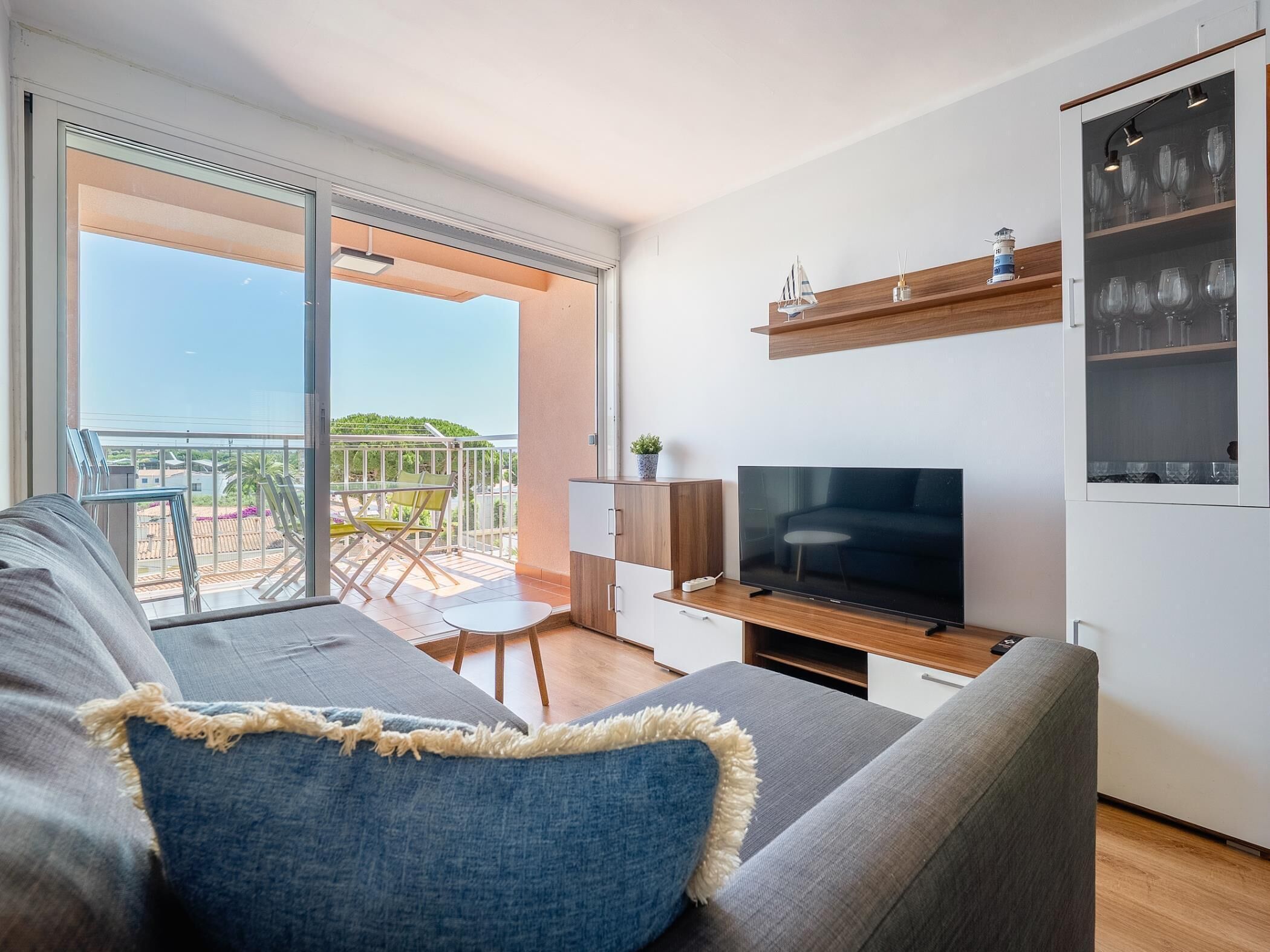 A modern living room with a large flat-screen TV, a sofa, a small table, and a balcony with a view.