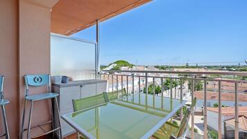 En balkon med et glasbord, stole, et hvidt skab og udsigt over en by.