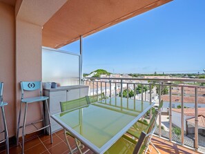 A balcony with a glass table and chairs, a white cabinet, and a view of a cityscape. - Apartment with terrace 400m beach (Cambrils)