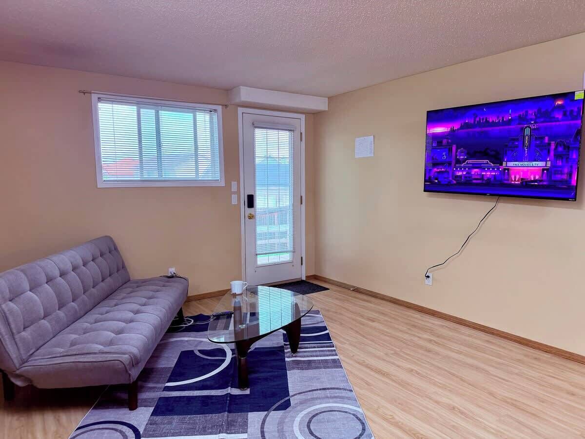 Ein Wohnzimmer mit einer Couch, einem Glastisch, einem an der Wand befestigten Fernseher und einer Tür mit Fenster.