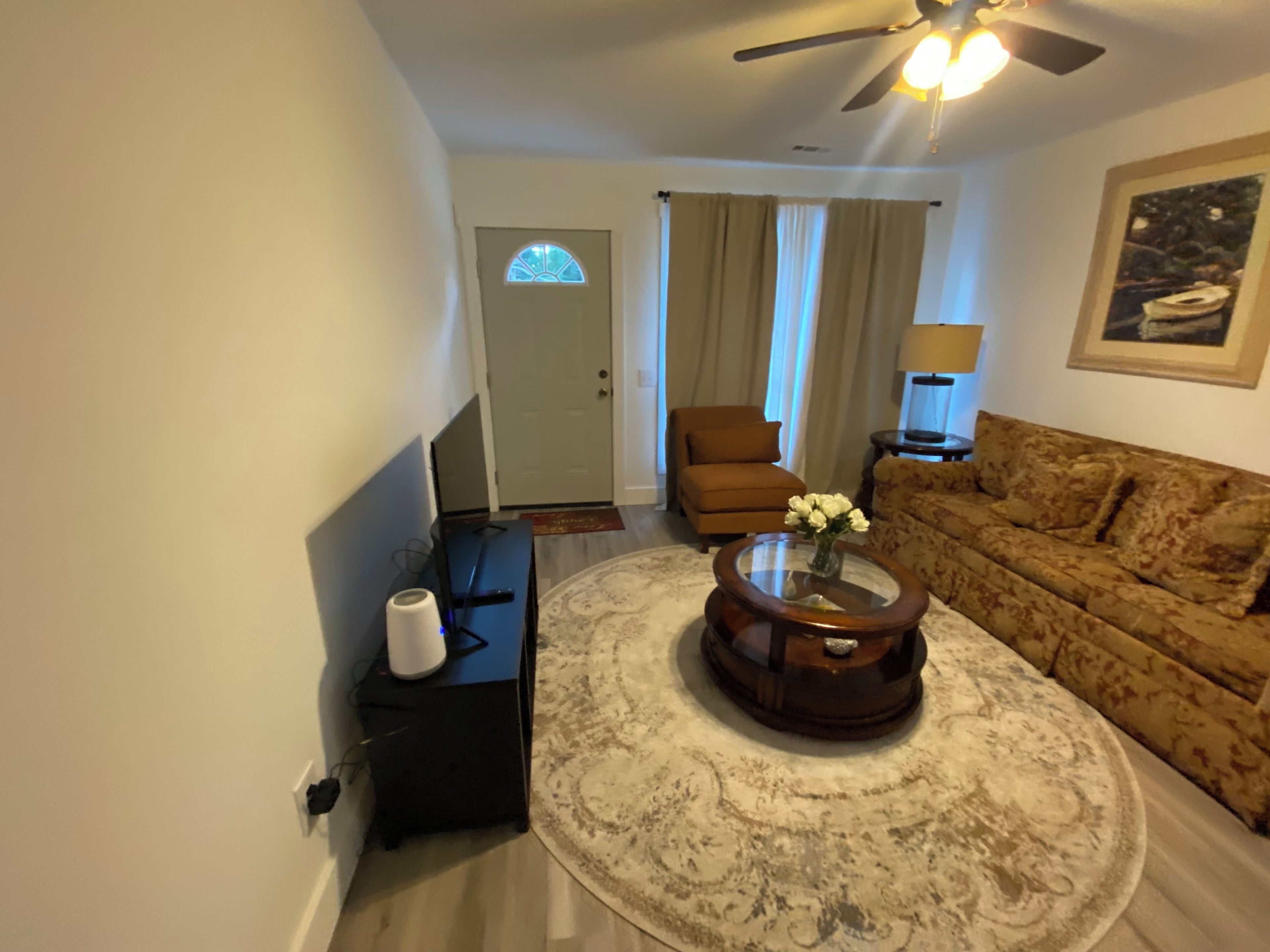 Ein Wohnzimmer mit einer Couch, einem Couchtisch mit einer Vase, einem Deckenventilator und einer Tür im Hintergrund.