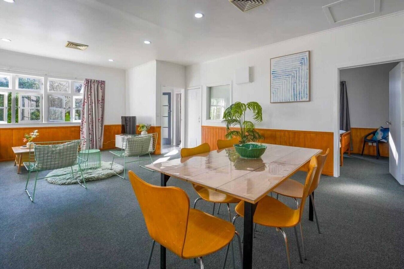Une pièce avec une grande table, des chaises, une plante et une fenêtre avec des rideaux.