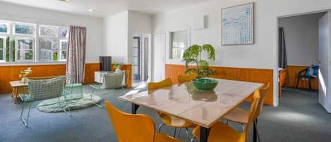 Une pièce avec une grande table, des chaises, une plante et une fenêtre avec des rideaux.
