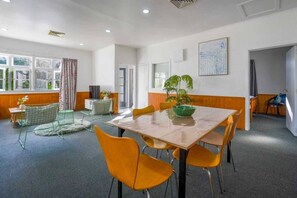 Une pièce avec une grande table, des chaises, une plante et une fenêtre avec des rideaux.