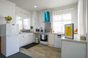 A compact kitchen with white cabinets, a stove, a microwave, and a dishwasher. - Classic 3-Bedroom Home in Whangarei (Whangārei)