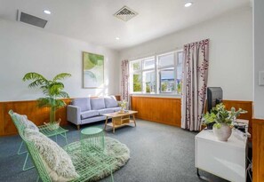 Quarto com sofá, uma cadeira, uma mesinha, televisão e uma planta.