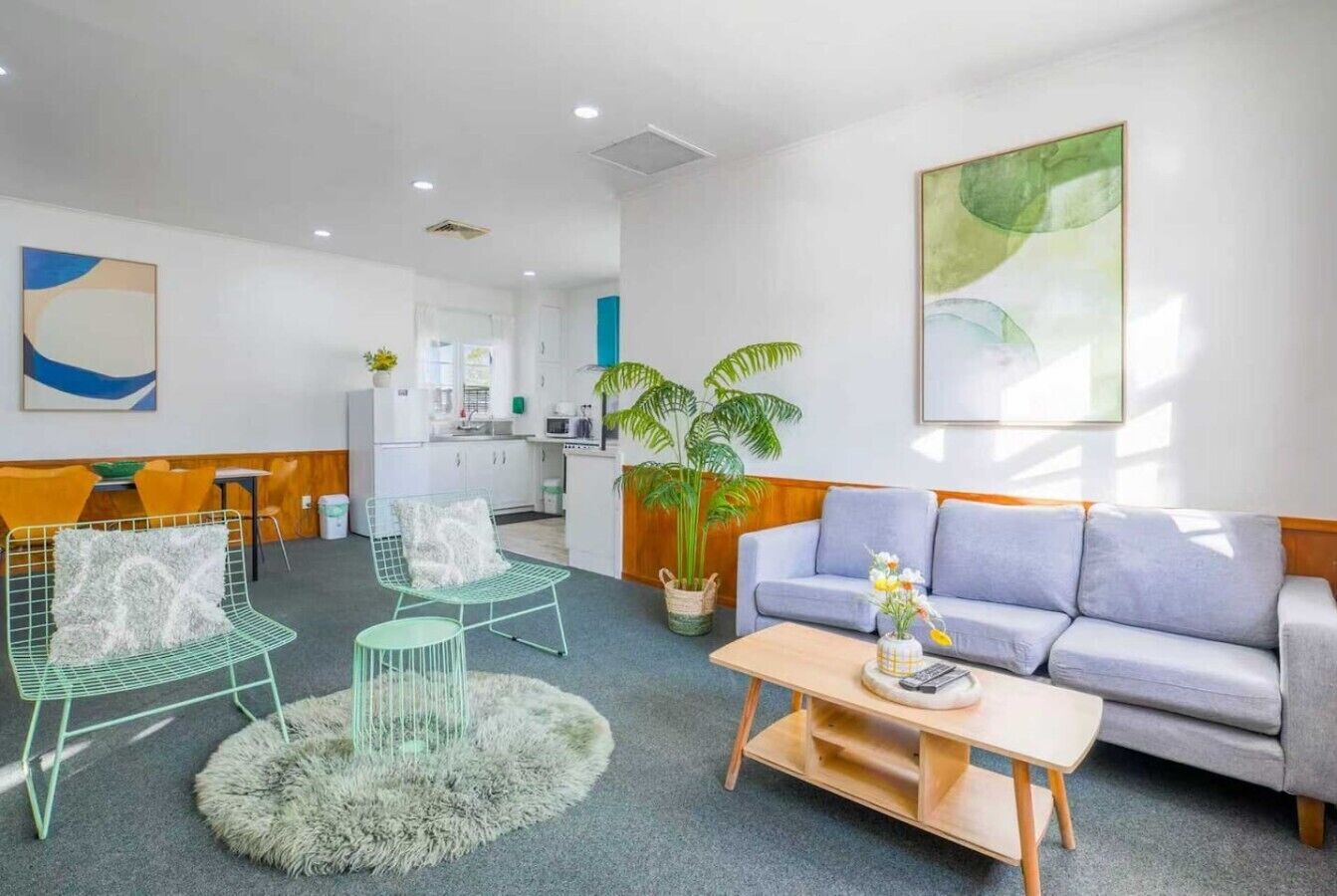 Ein modernes Wohnzimmer mit einem grauen Sofa, zwei grünen Gestellstühlen, einem runden Couchtisch und einer großen Topfpflanze.
