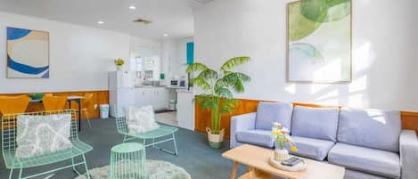 A modern living room with a grey sofa, two green wireframe chairs, a round coffee table, and a large potted plant.