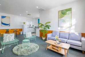 A modern living room with a grey sofa, two green wireframe chairs, a round coffee table, and a large potted plant. - Classic 3-Bedroom Home in Whangarei (Whangārei)