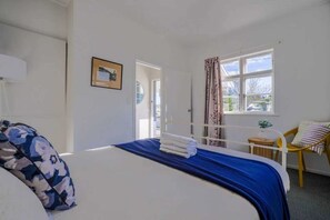 A bedroom with a bed, a chair, a window with curtains, and a door leading outside. - Classic 3-Bedroom Home in Whangarei (Whangārei)