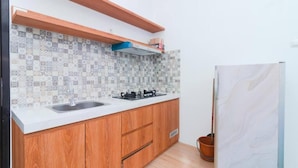 A kitchen with a tiled backsplash, wooden cabinets, a white countertop, and a built-in stove. - Cozzy Villa Ree (batu)
