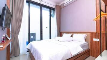 Quarto de hotel com uma cama, televisão, janela com cortinas e ar condicionado.