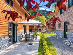 Ein Holzgebäude mit einer Terrassenfläche, inklusive Tisch und Stühlen unter einem weißen Sonnenschirm.