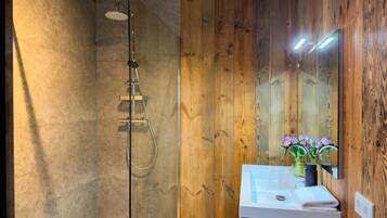 A modern bathroom with a glass-enclosed shower, wooden panel walls, a white sink with a mirror, and a vase with flowers.