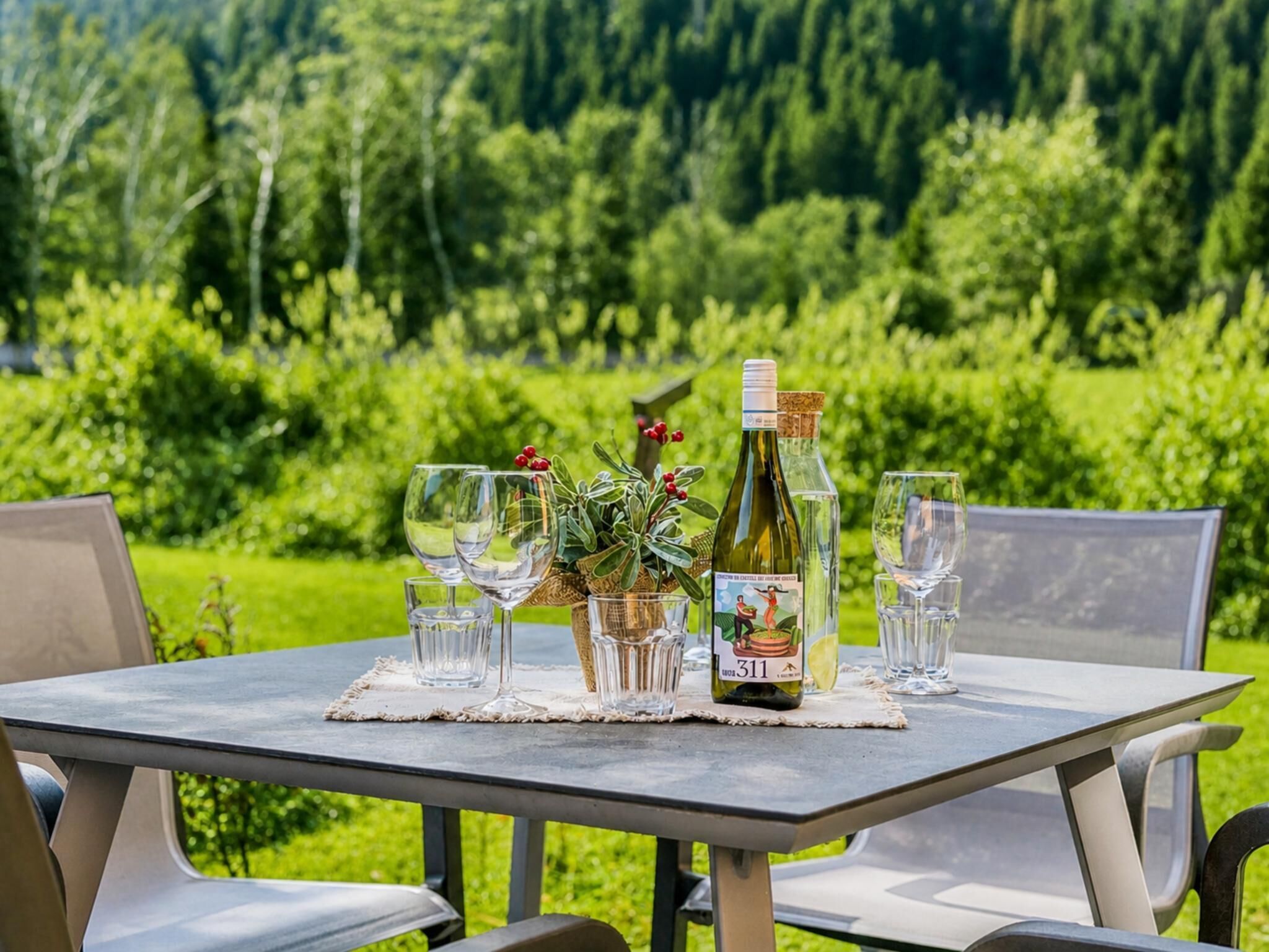 A table set outdoors with a bottle of wine, glasses, and a small plant.