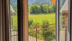 Blick von einem Balkon mit Metallgeländer auf ein grünes Feld und ferne Berge.
