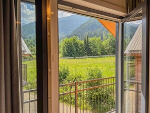 Blick von einem Balkon mit Metallgeländer auf ein grünes Feld und ferne Berge.