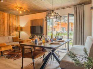 Ein modernes Wohnzimmer mit einer Holzvertäfelung, einer Couch, einem Esstisch mit Stühlen und einem großen Fenster mit Vorhängen.